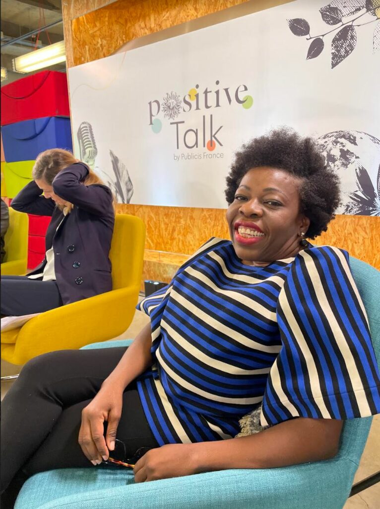 Deza, femme noir assise avec son beau sourire sur une chaise. Derrière une affiche "positive Talk"