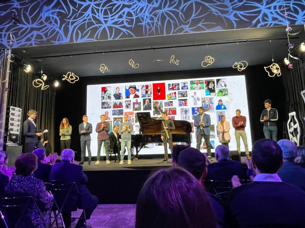 Image capturée lors de l'évènement de la fondation Banque Populaire pour leur 25e anniversaire dépeint une scène animée avec une foule joyeuse. 
Au centre un monsieur joue du piano, créant une ambiance festive. Un présentateur anime l'évènement, ajoutant une touche de célébration à cette commémoration mémorable. 